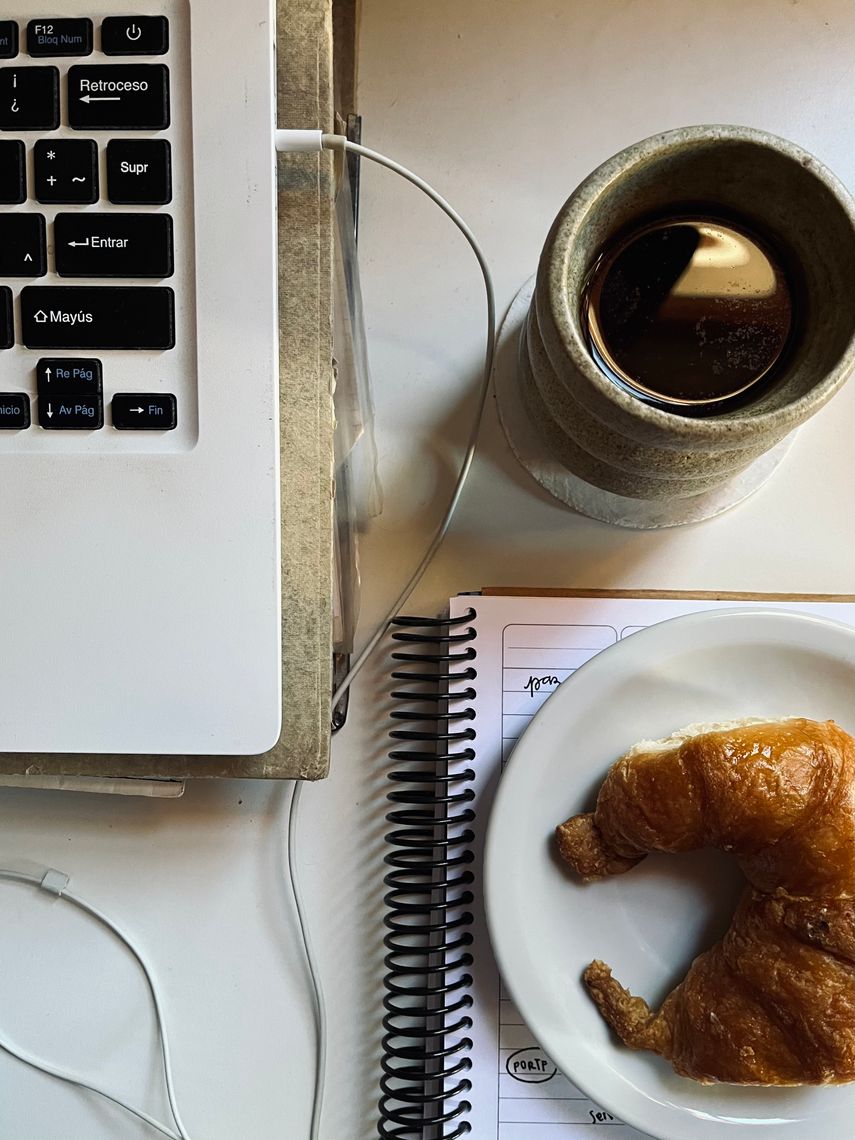 flat lay with a computer, notebook, croissant and coffee