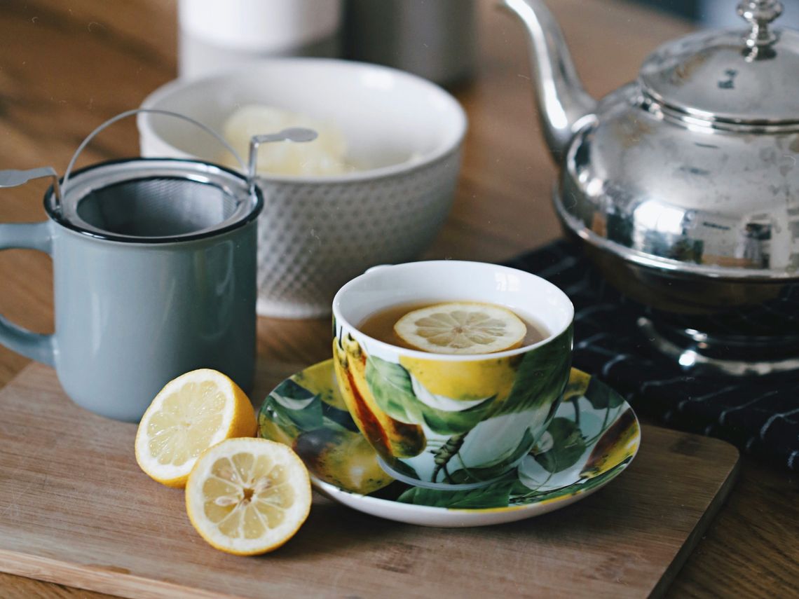 gray teapot beside mug filled with tea and lemon