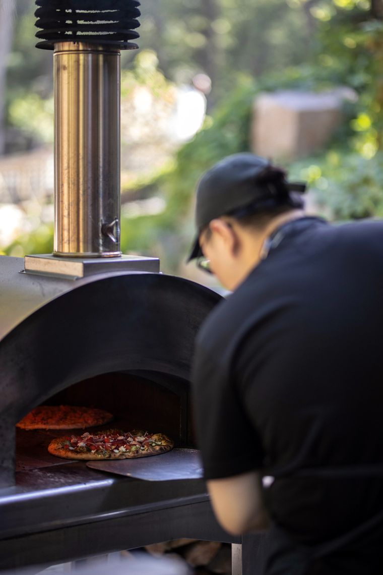 employee sliding a pizza in a wood oven