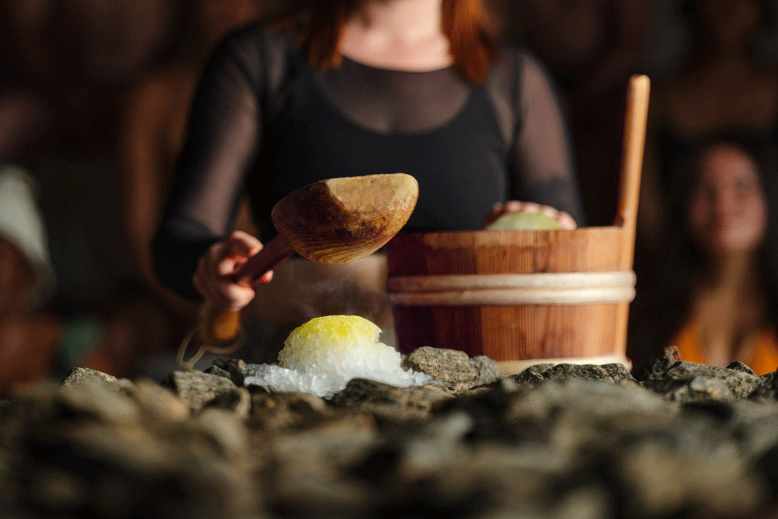 Artisan smashing an infused snowball onto a hot sauna stove