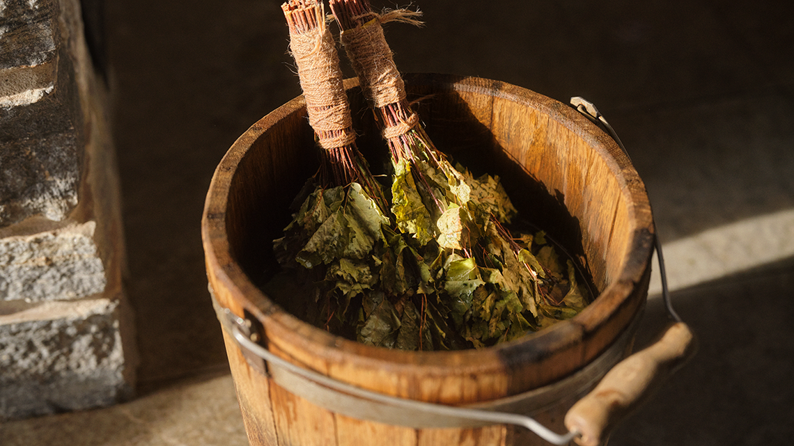 Birch branches in a bucket next to a sauna stove